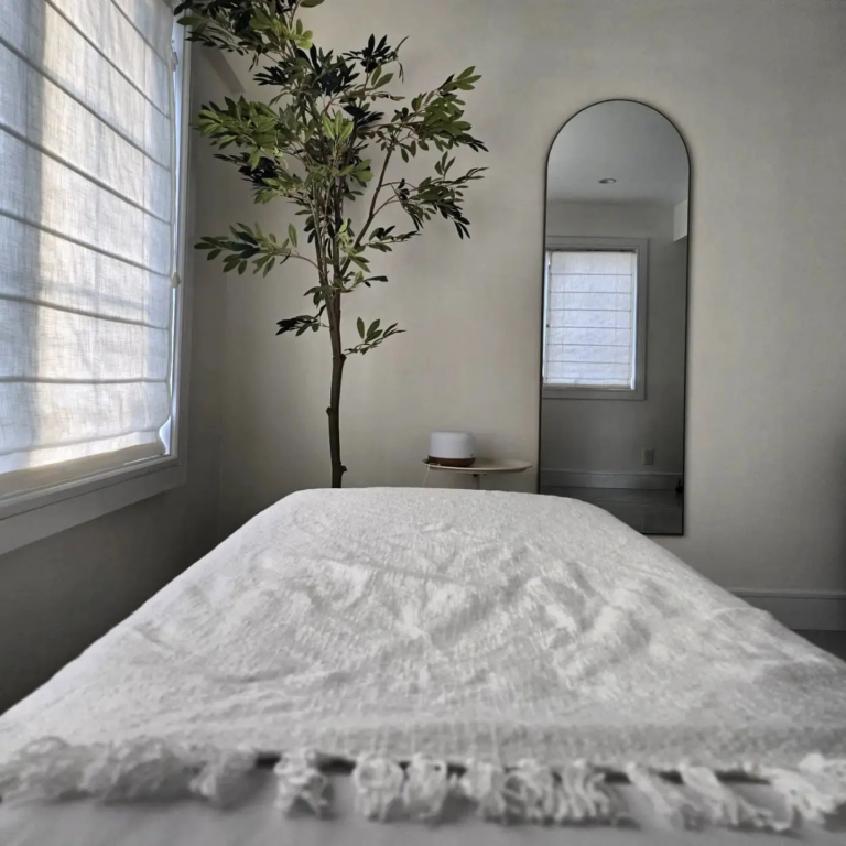 there is a bed with a white blanket and a tree in the corner